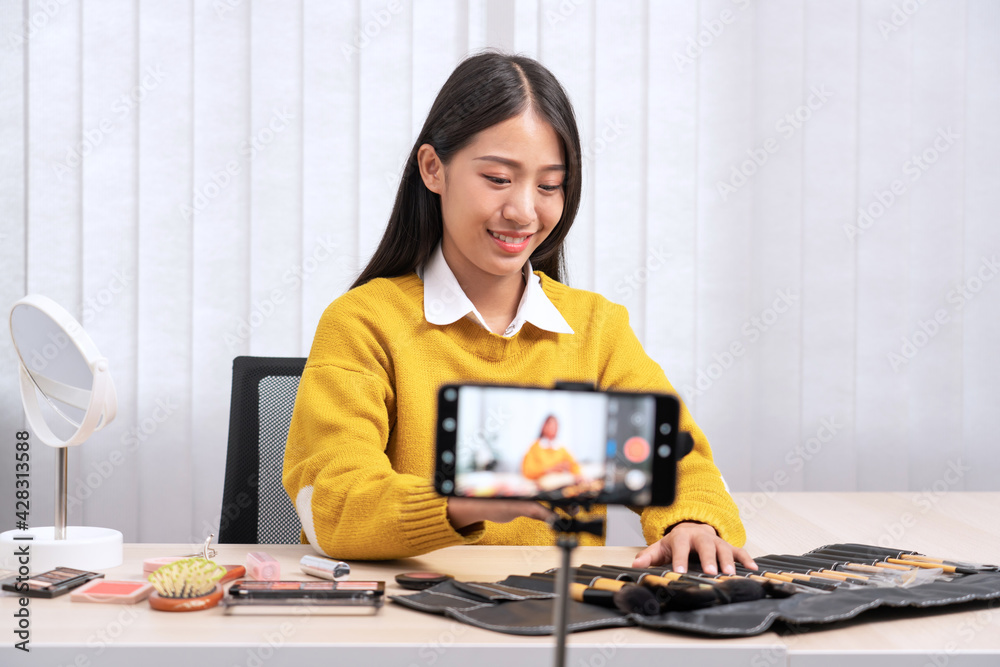 Beautiful asian woman blogger using camera phone recording vlog video live streaming and applying makeup for review cosmetics at home Beautiful asian woman blogger using camera phone recording vlog video live streaming and applying makeup for review cosmetics at home