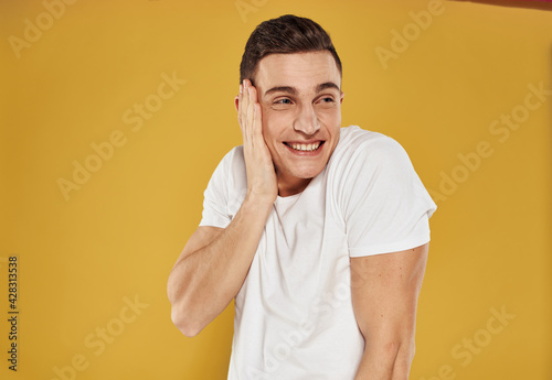 Cheerful man holds his hand near the face on a yellow background emotions joy model