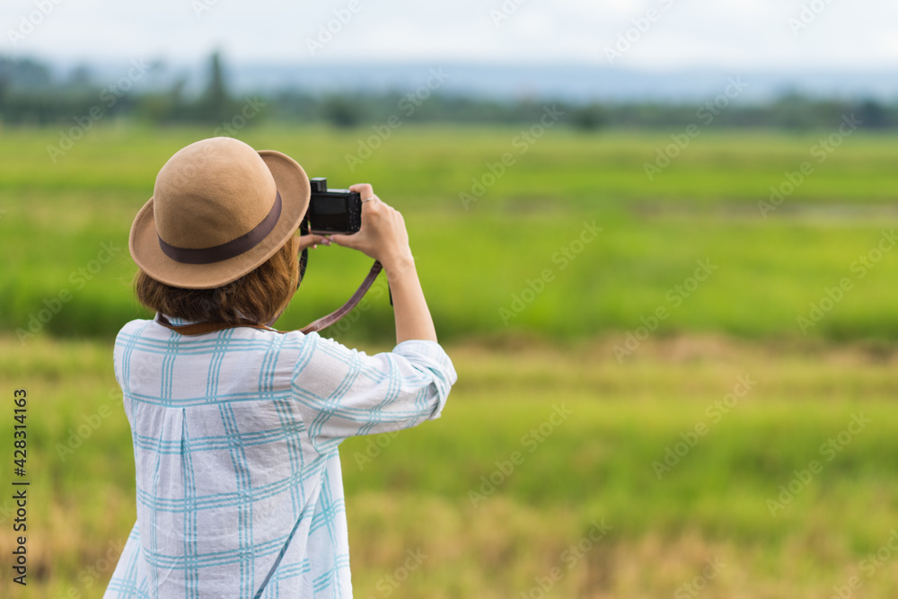 A tourist woman enjoy taking photo of landscape during her summer vacation holiday in the greenery field. A stylish traveler woman in hat taking photo of herself and landscape while relaxing A tourist woman enjoy taking photo of landscape during her summer vacation holiday in the greenery field. A stylish traveler woman in hat taking photo of herself and landscape while relaxing