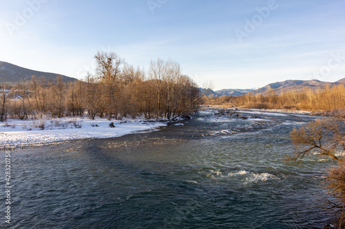 Winter in the foothills, an ice-free river on a frosty morning in the rays of the rising sun.