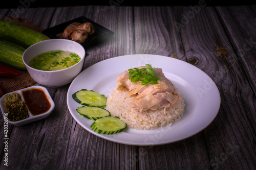 Hainanese chicken rice or Khao Man Gai Asian food in a wood white plate with delicious broth and dipping sauce.