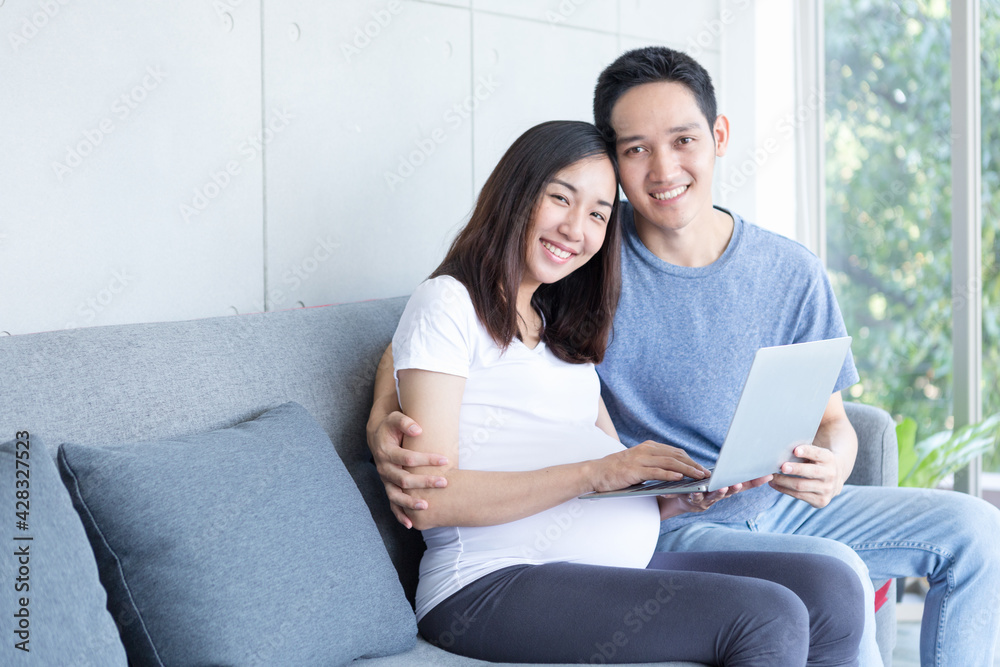 An expectant mother and father are sitting in the living room with a laptop computer.. An expectant mother and father are sitting in the living room with a laptop computer..