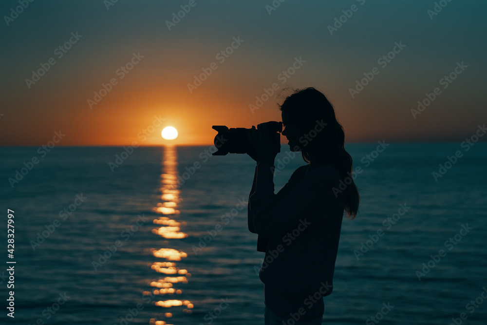 woman photographer with camera at sunset near the sea on the beach
