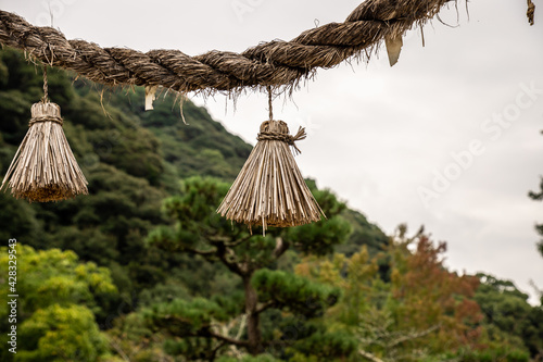 Japanese Shimenawa with Onusa (Haraikushi) hanged traditional torii gate in Shinto shrine. An Onusa (Nusa) is a wooden wand used in Shinto rituals. Asian oriental, zen, rural, nostalgia concept © Koshiro