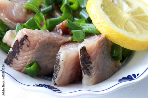 Pieces of salted herring fish on a plate with green onion and lemon slice. Swedish pickled herring on wooden table background. Midsummer traditional food. Top view, copy space	 photo