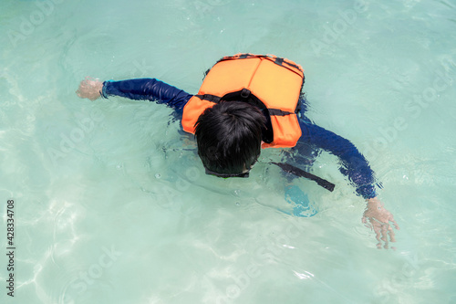 Asia child boy wearing goggles, swimming suit and life jacket snorkelling in the sea at beach in Thailand with copy space. Summer vacation and holiday travel. Relaxation and happy in the water