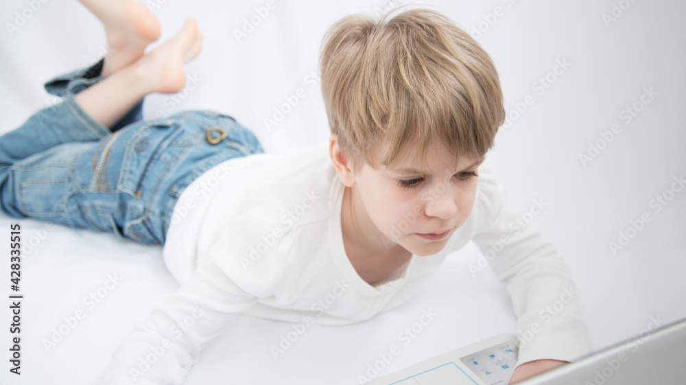 The blond child looks attentively at the computer or laptop screen. Close-up portrait The blond child looks attentively at the computer or laptop screen. Close-up portrait