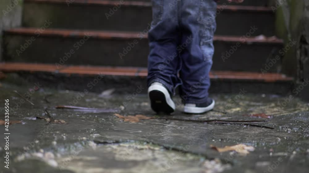 Toddler boy splashes into puddle of water. Child plays with puddles Toddler boy splashes into puddle of water. Child plays with puddles