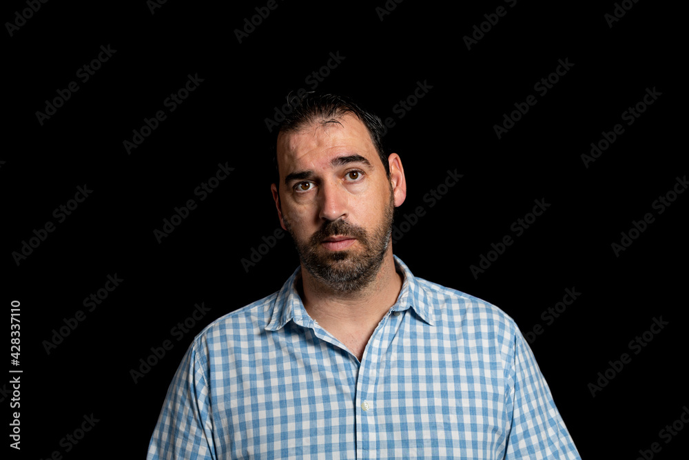 Portrait of bearded man dressed in white and blue plaid shirt posing worried isolated on black studio background