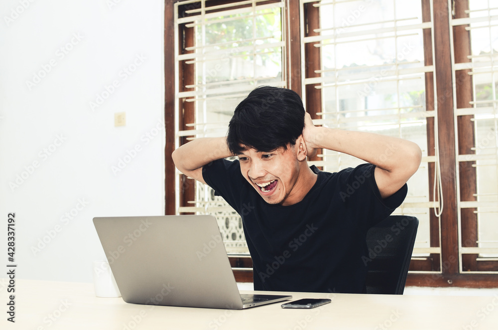 Fototapeta premium The man in black Asian t-shirt sat in front of the laptop with a very happy expression