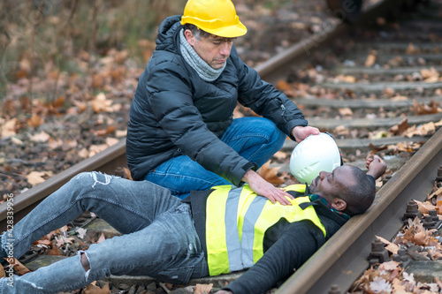 African American railroad engineer injured in an accident at work on the railway tracks. Coworker helping him
