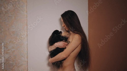 Young nudist woman holding her funny licking little spitz dog photo