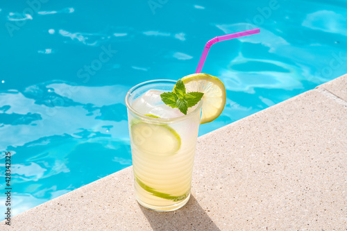 Fresh lemonade or mojito cocktail in glass with straw on a swimming poll border on sunny day