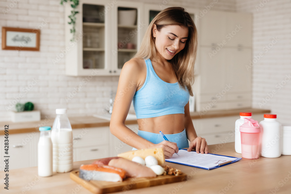 Pleasant younf woman writing tips for healthy nutrition in kitchen Pleasant younf woman writing tips for healthy nutrition in kitchen