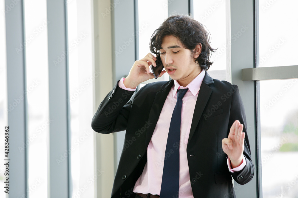 Asian entrepreneur speaking on smartphone near window Asian entrepreneur speaking on smartphone near window