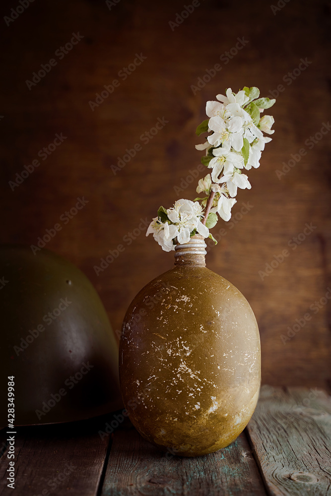 A sprig of an apple tree in a soldier's flask on a brown background. Photo by May 9