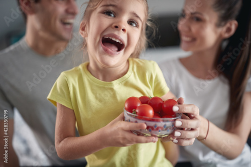 A little girl with her parents posing for a photo with a bowl full of cherry tomatoes at home. Family  breakfast  together  home