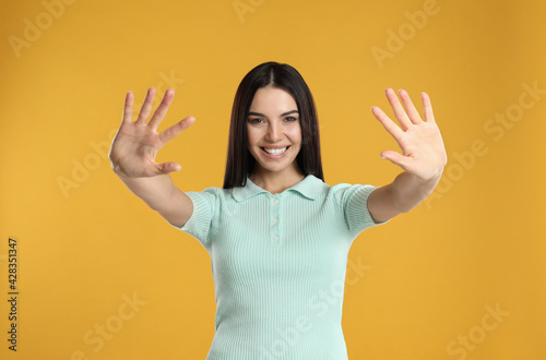 Woman showing number ten with her hands on yellow background