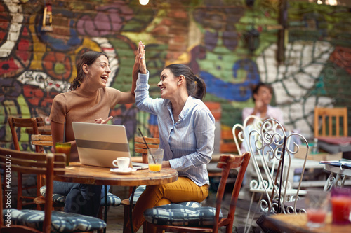 Two cheerful female students are laughing while spending a free time in bar's garden together. Leisure, bar, friendship, outdoor