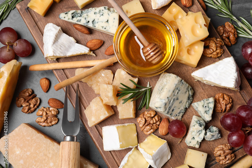 Cheese plate with honey, grapes and nuts on grey table, flat lay