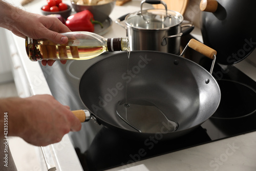 Man pouring cooking oil into frying pan in kitchen  closeup