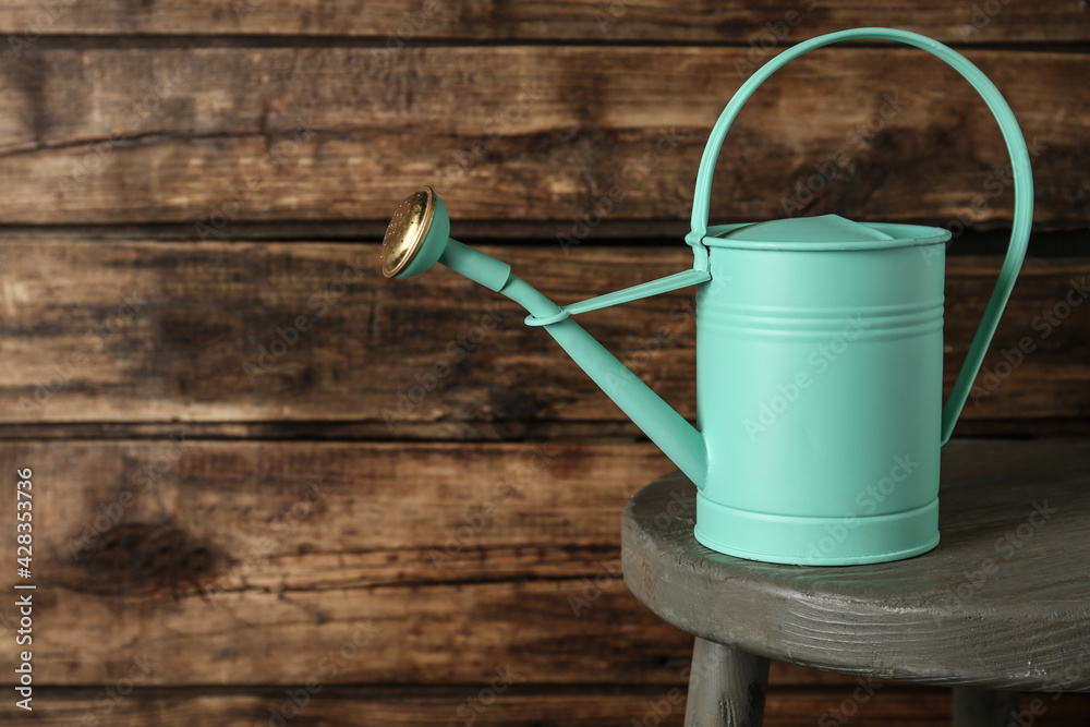 Turquoise metal watering can on table against wooden background, space for text