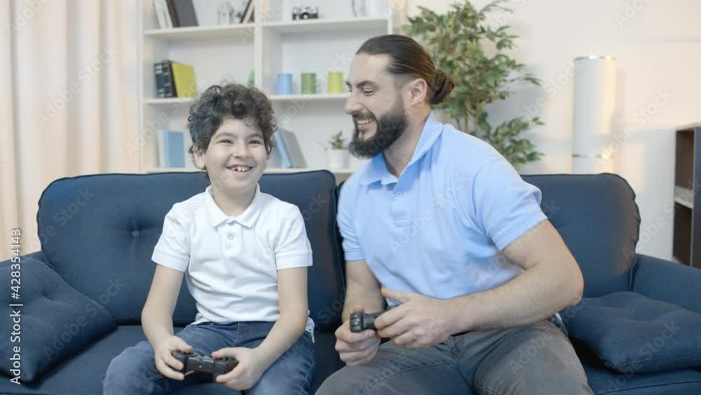 Excited father and son playing video game, high-fiving to celebrate victory Excited father and son playing video game, high-fiving to celebrate victory