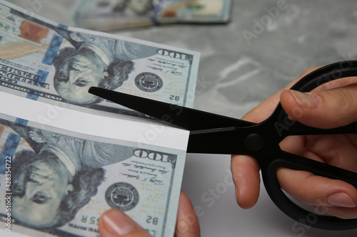 Photos Counterfeiter cutting dollar banknotes with scissors at grey marble table, closeup