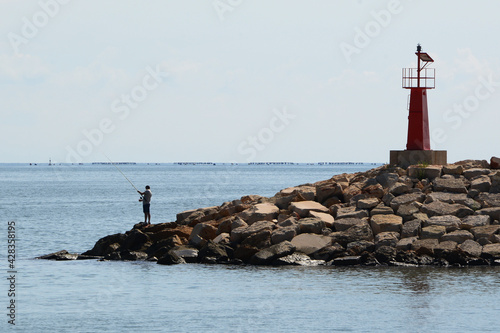 Hombre pescando en la punta de las rocas, con un pequeño faro a su espalda. 