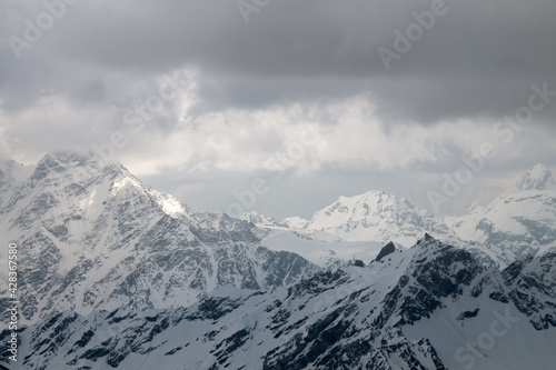 Multi-layered fluffy clouds high above the snow-capped mountain peaks with rays of light shining through them. Mountain tele landscape. Non-contrasting background for travel and banners
