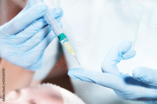 Young caucasian woman doctor dripping a drop of vaccine or injection from a syringe onto a gloved finger. Vaccinations and injections in cosmetology and medicine