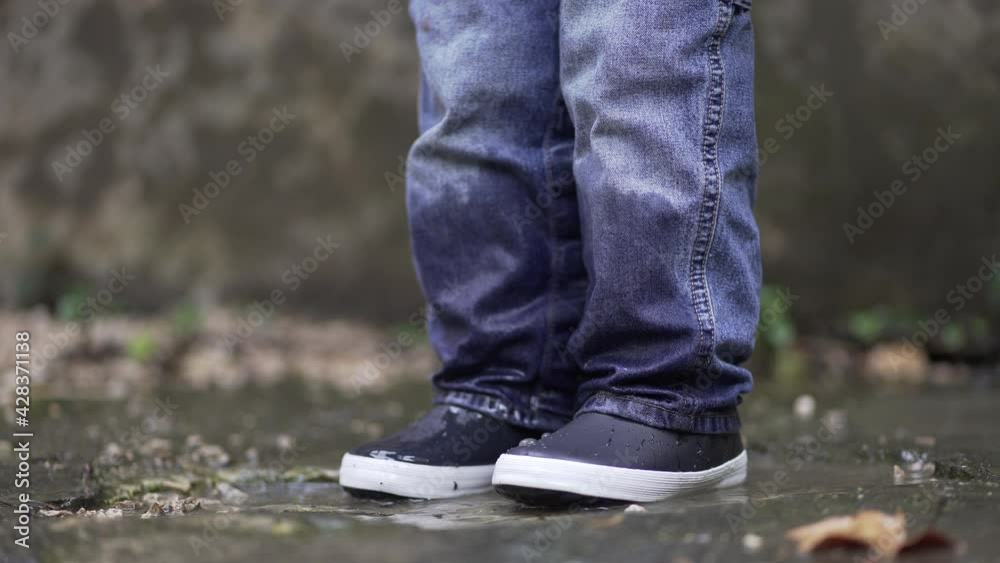 Toddler boy splashes into puddle of water. Child plays with puddles Toddler boy splashes into puddle of water. Child plays with puddles