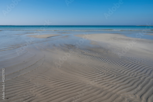 Sabbia bianca con mare trasparente e cielo azzurro.
