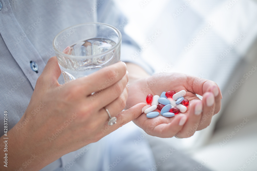 Enough pills to overdose a person held in a hand of woman with a glass of water in the other hand Enough pills to overdose a person held in a hand of woman with a glass of water in the other hand