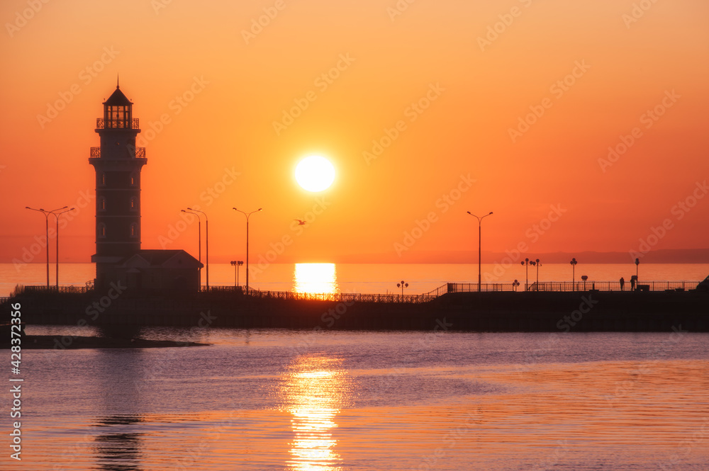 lighthouse silhouette at red and orange sunset colours with sun and bird