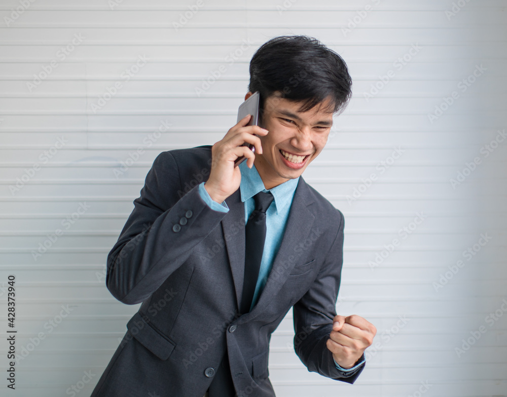 Asian businessman speaking on smartphone and celebrating success Asian businessman speaking on smartphone and celebrating success