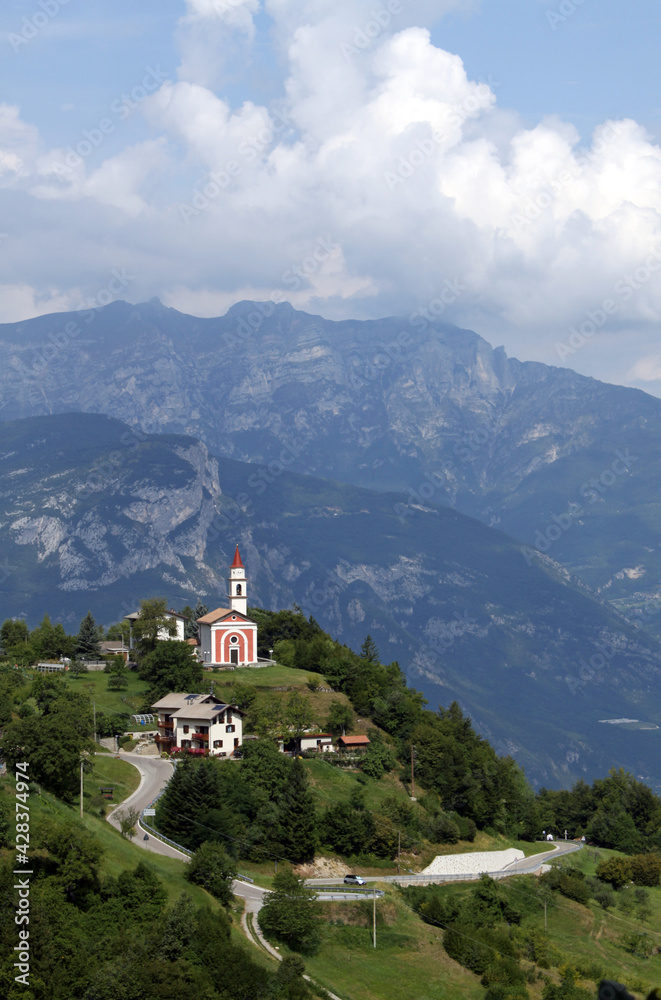 Green and blue mountain landscape with a small red church in Guardia, Trentino, Italy