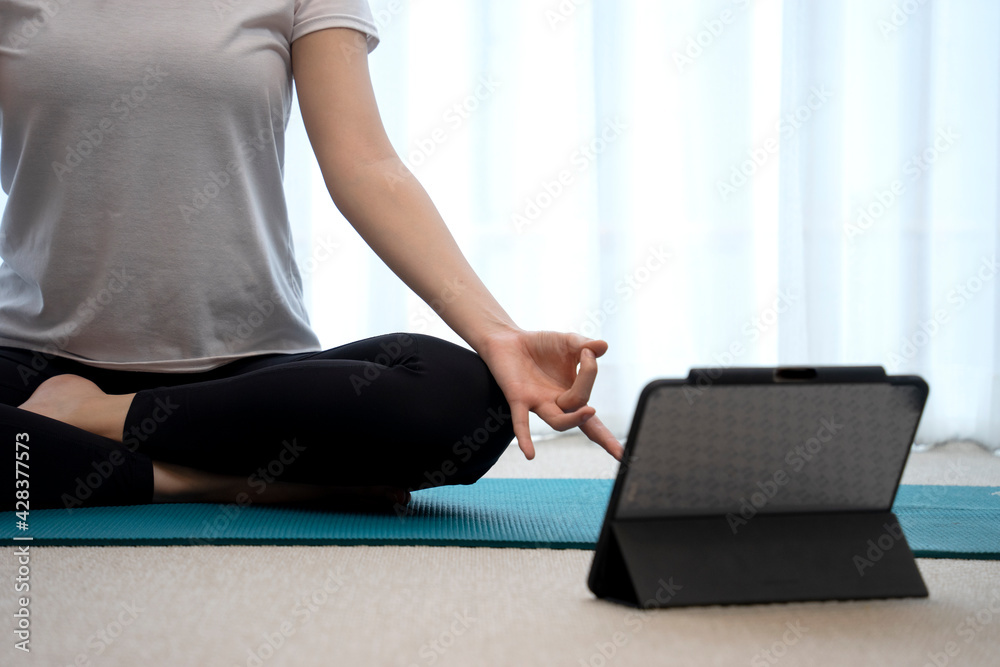 Naklejka premium The young lady is meditating on a mat with a tablet placed