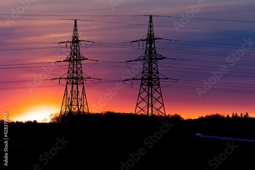 Electricity poles at sunset. High voltage grid towers with wire cable at distribution station.