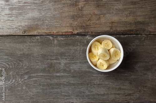 Slices of bananas in a white plate on a rustic wooden background preparing for cooking with copy space.