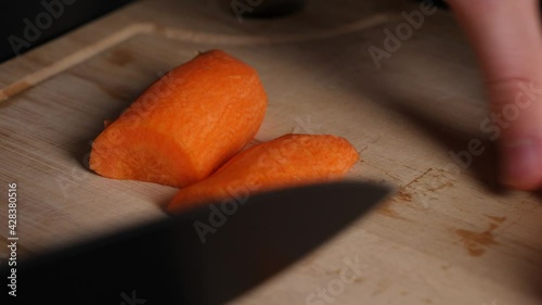 Chef hands cuts carrots pieces in half on wood chopping board. photo