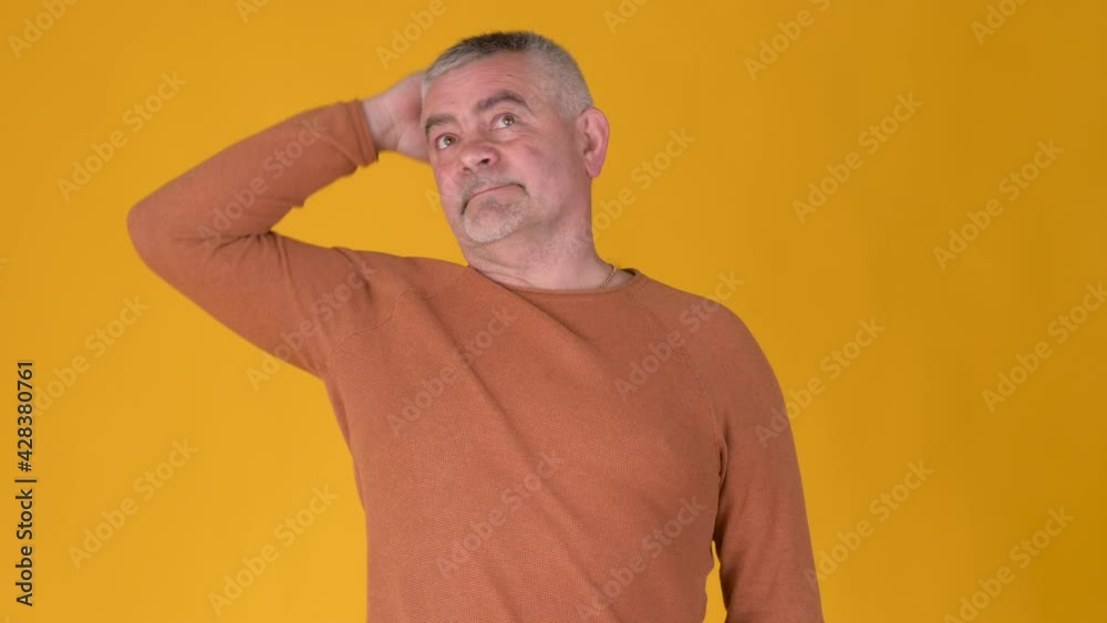 Portrait elderly gray-haired man thinking over difficult choice against a yellow studio background. People pondering idea looking puzzled