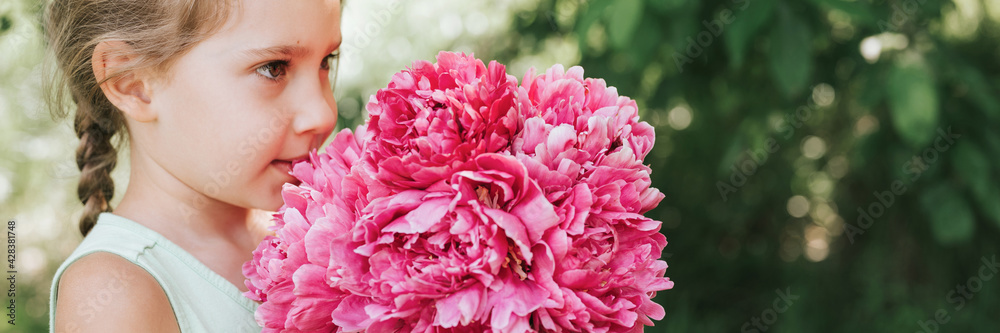 portrait of a happy cute little caucasian seven year old kid girl, holds in hands and smell and enjoying a bouquet of pink peony flowers in full bloom on the background of nature. banner portrait of a happy cute little caucasian seven year old kid girl, holds in hands and smell and enjoying a bouquet of pink peony flowers in full bloom on the background of nature. banner