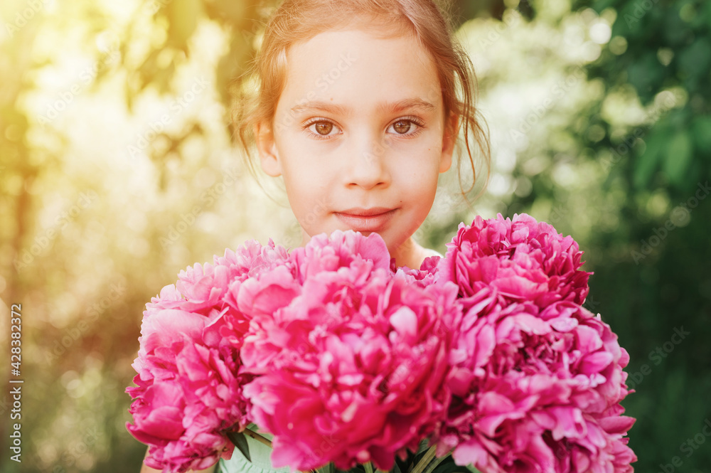 portrait of a happy cute little caucasian seven year old kid girl, holds in hands a bouquet of pink peony flowers in full bloom on the green background of nature. flare portrait of a happy cute little caucasian seven year old kid girl, holds in hands a bouquet of pink peony flowers in full bloom on the green background of nature. flare