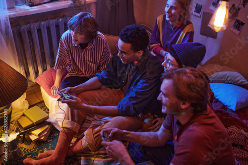 Group of friends sitting on the floor in dark room using joysticks while playing video game at a party