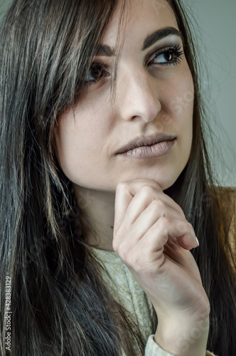 Portrait of a beautiful young successful woman with long brown hair touching her chin while looking intently thinking