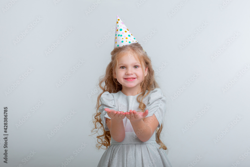 little girl in birthday hat blowing confetti on white studio background