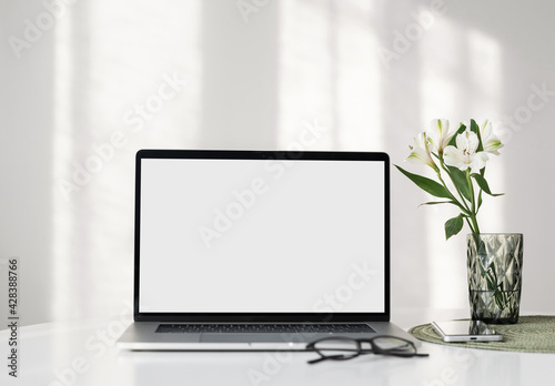 Laptop computer with empty blank mockup screen over white modern living room design. Work place, home office interior. Business, web site advertisement, workspace concept