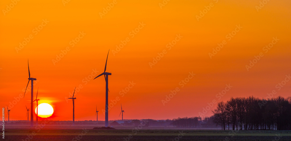 Obraz premium Wind turbines for renewable energy in an agricultural field in bright orange yellow sunlight at sunrise in spring, Almere, Flevoland, The Netherlands, April 17, 2021