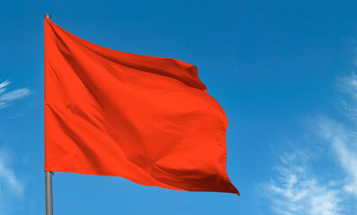 Bright red flag waving against blue sky, blank red banner